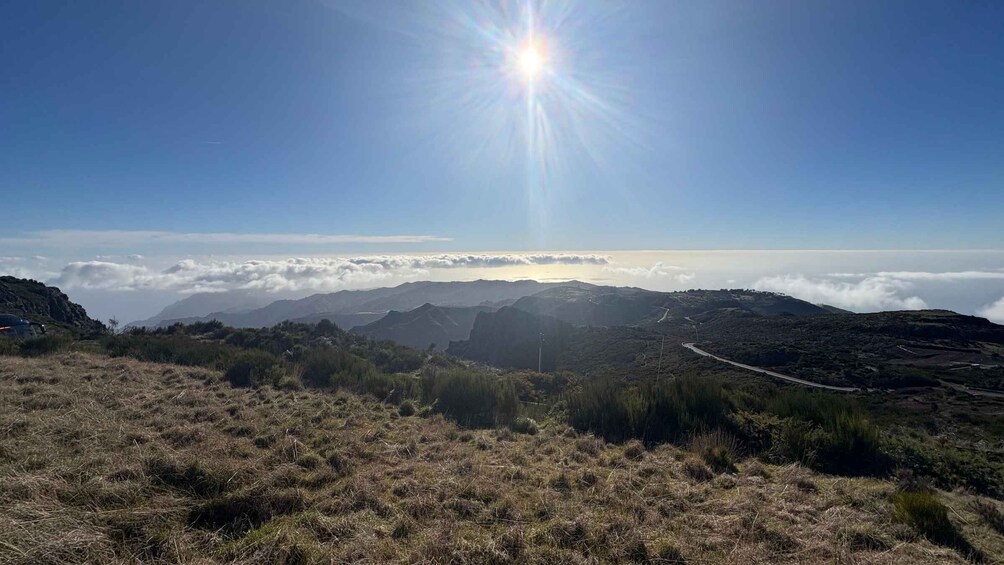 A mountainous landscape with a clear sky, a road winding through the terrain, and a sun shining brightly. 1
