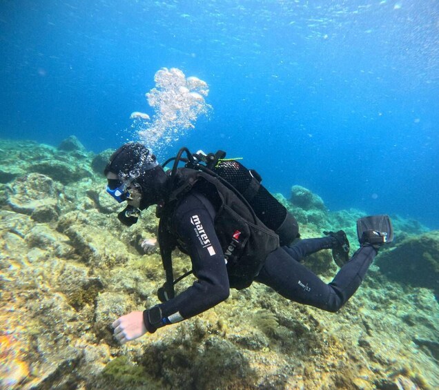 A diver underwater with a backpack and fins, surrounded by rocky terrain. 2