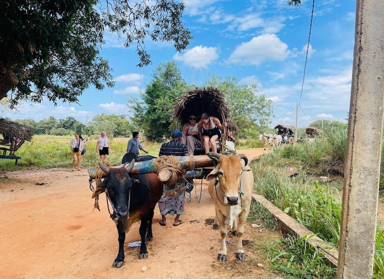 A group of people riding on a wooden cart pulled by two oxen on a dirt road. 1