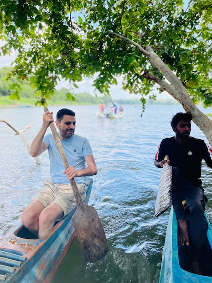 Two people rowing a boat on a calm body of water, surrounded by trees. 3