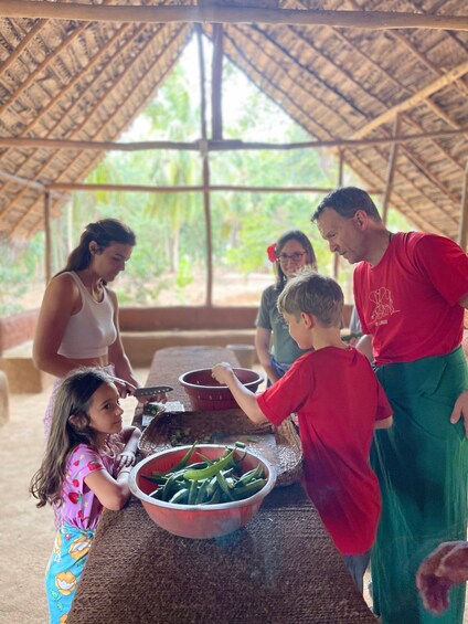 A group of people preparing food in a thatched-roof structure with large windows. 2