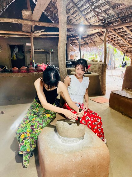 Two people engaged in pottery making, with a rustic setting featuring a thatched roof and traditional pottery wheels. 3