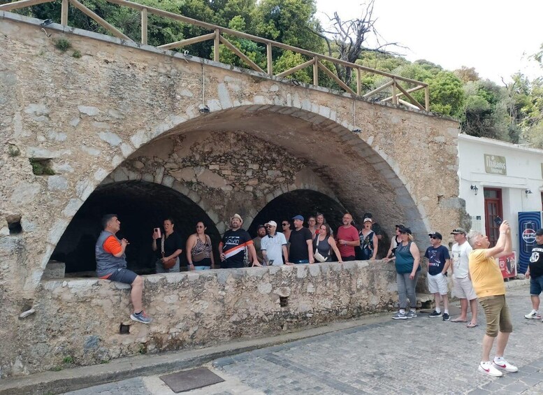 A group of people standing and sitting by an ancient stone bridge with arched openings. 5