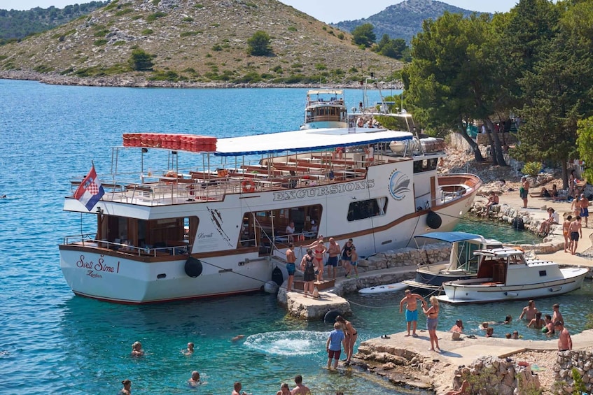 A large boat docked at a pier with people swimming and sunbathing nearby. 1