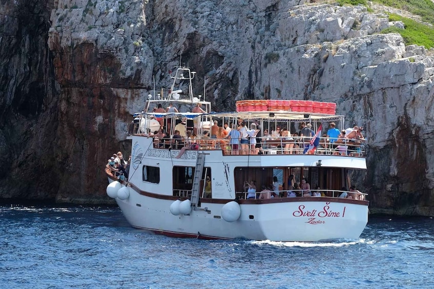 A boat named 'Sveti Sime I' with passengers and a rocky cliff in the background. 5
