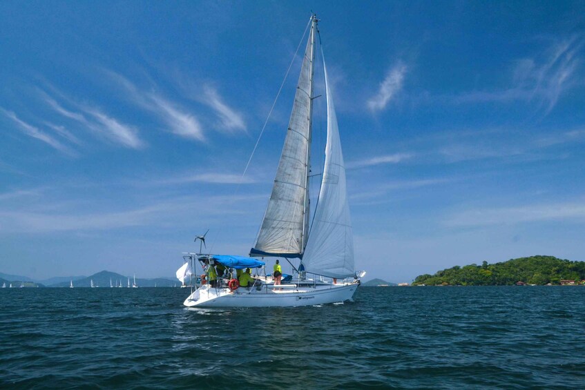 A sailboat with a crew on a calm sea, surrounded by other boats and a distant island. 3