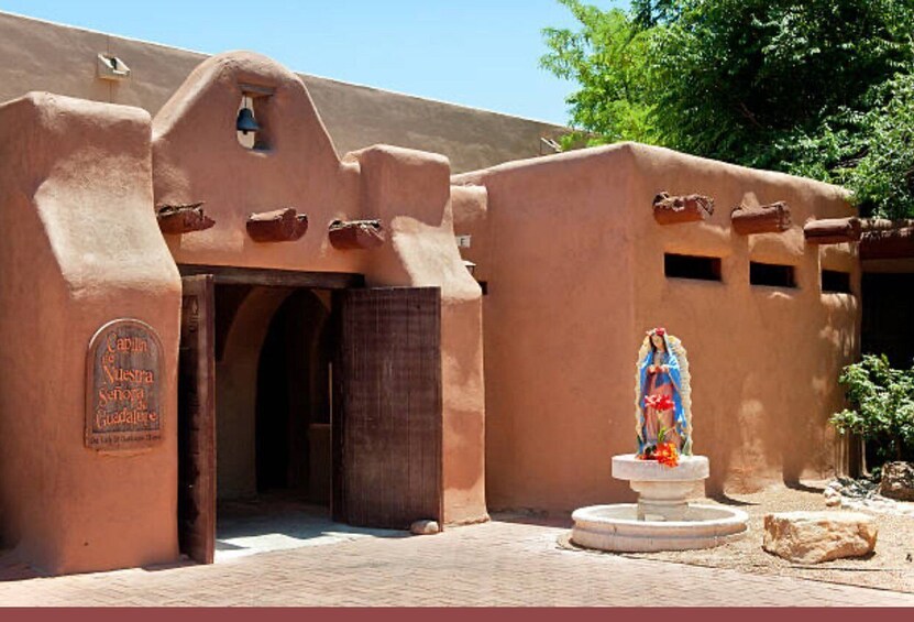 A traditional adobe building with a bell tower and a statue of the Virgin Mary. 3