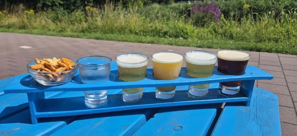 A blue table with six glasses of beer and a bowl of crackers. 2