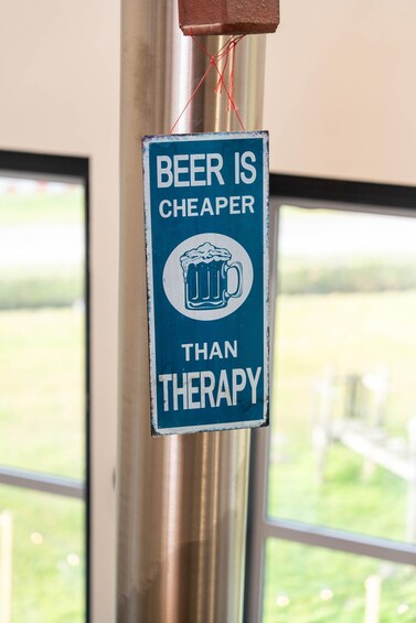 A sign with a beer mug icon and text stating 'BEER IS CHEAPER THAN THERAPY' hanging on a metal pole. 4