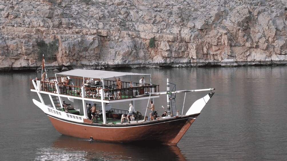 A brown boat with multiple levels, docked near a rocky shoreline. 3
