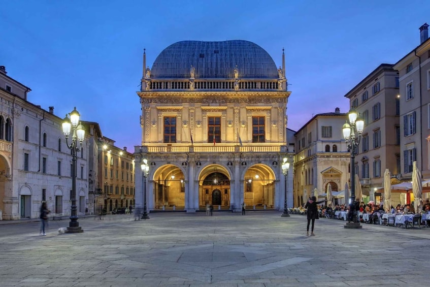 A historic building with a large dome and arched entrances, surrounded by a plaza with outdoor seating and street lamps. 2