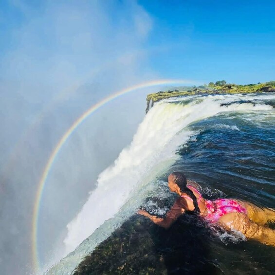 A waterfall with a rainbow and a person swimming. 5