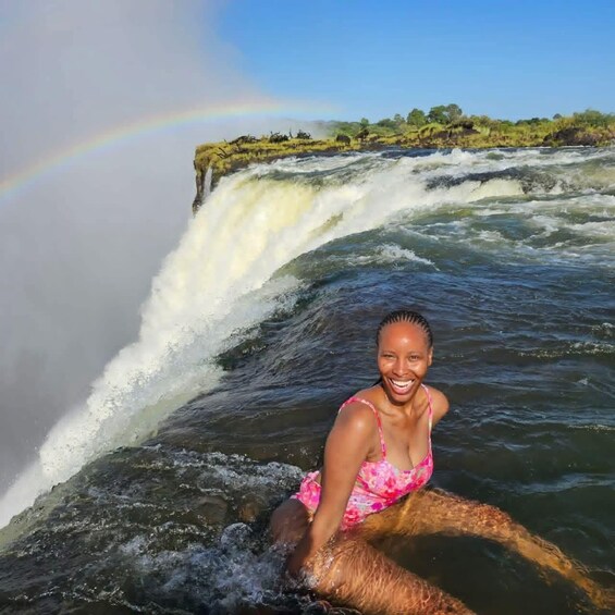 A waterfall with a rainbow, a person in a pink swimsuit, and a natural landscape. 4