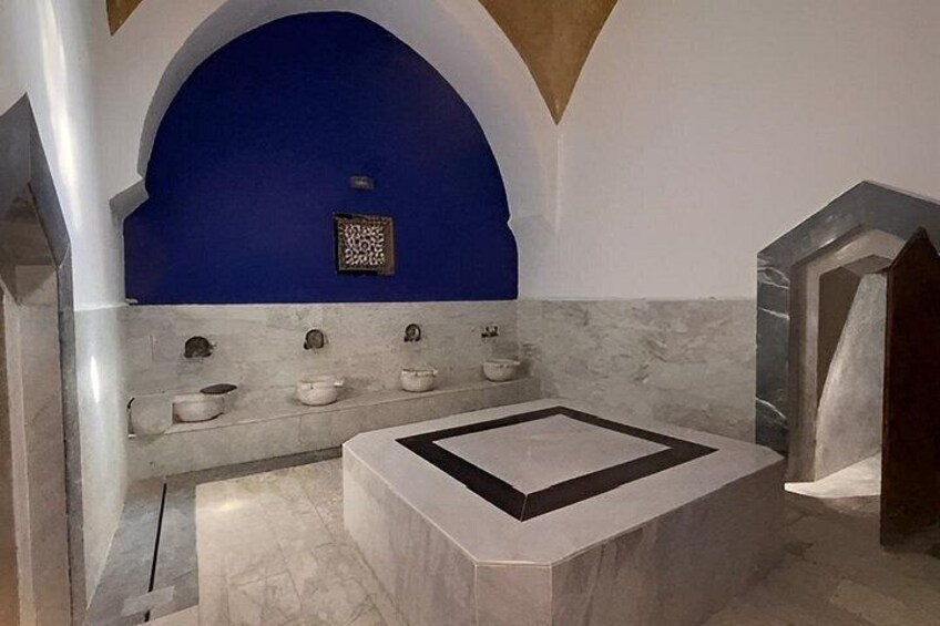 A bathroom with a blue wall, a marble floor, and a geometric design on the floor. 5