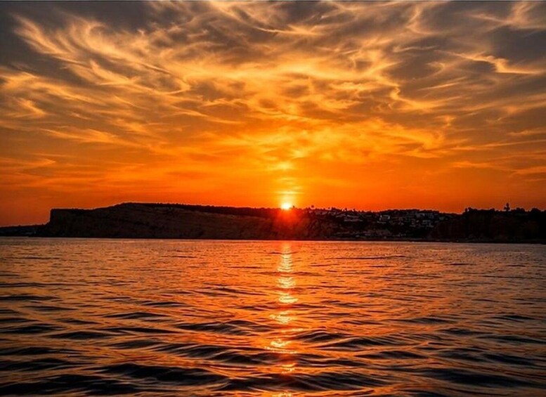 A sunset over a body of water with a distant shoreline and a hill. 1