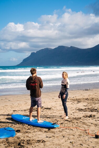Two people on a beach with surfboards, ocean waves, and mountains in the background. 2