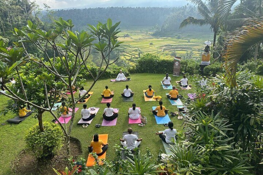 A group of people meditating outdoors on yoga mats in a lush, green landscape with a view of terraced fields in the background. 1