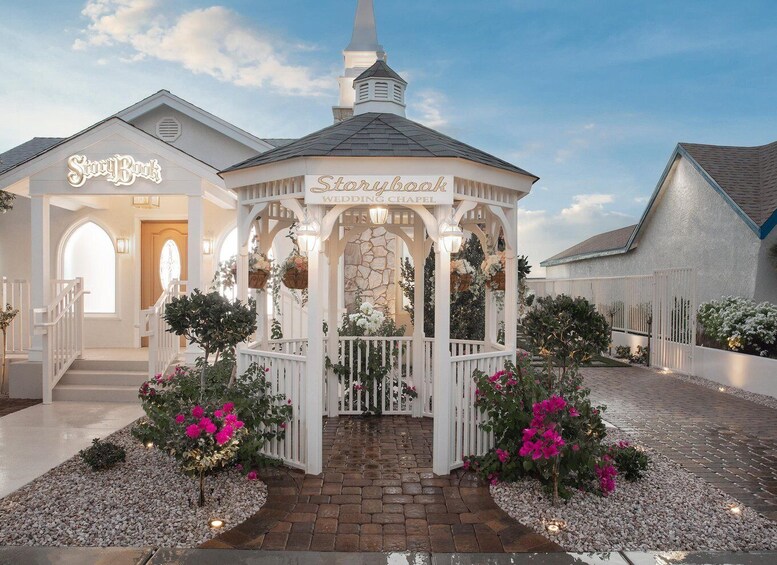 A Storybook Wedding Chapel with a white gazebo, surrounded by pink flowers and a stone pathway. 2