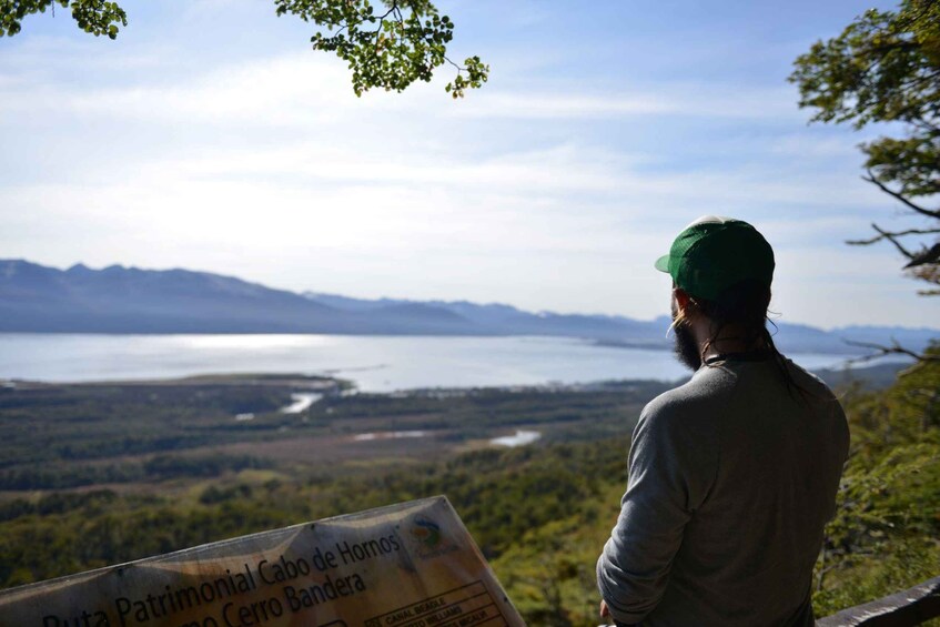 A person standing at a viewpoint overlooking a landscape with a sign reading "Ruta Patrimonial Cabo de Hornos Cerro Cero Bandera". 5