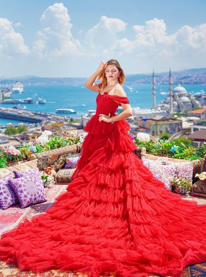 A woman in a red dress standing on a rooftop with a cityscape and a body of water in the background. 5