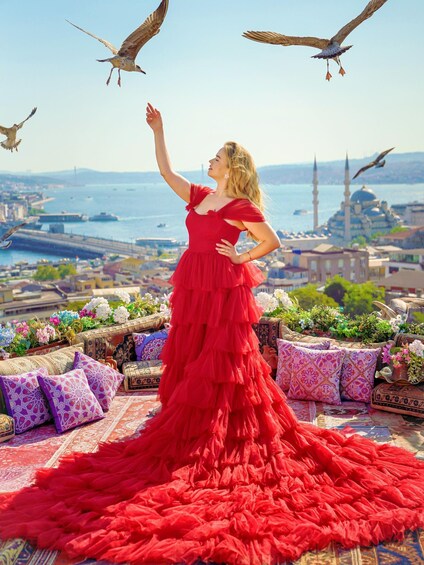 A woman in a red dress standing on a rooftop with a view of a cityscape and a mosque. 4