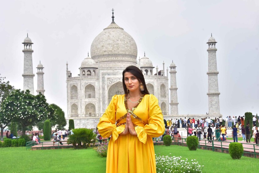 A person in a yellow dress standing in front of the Taj Mahal with a crowd in the background. 4