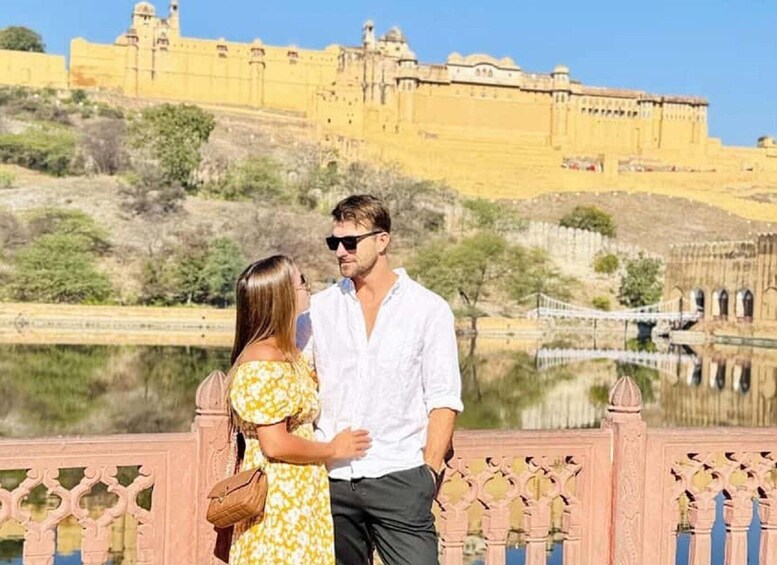 A couple standing by a reflective water body with a historic yellow fortress in the background. 3