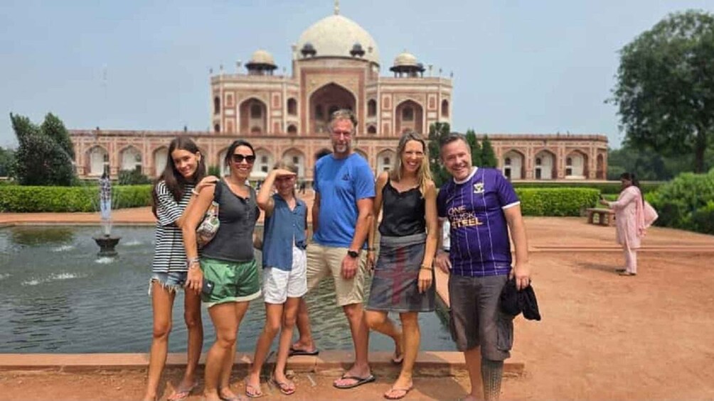 A group of people standing in front of a large, historic building with domes and arches, with a fountain in the foreground. 2