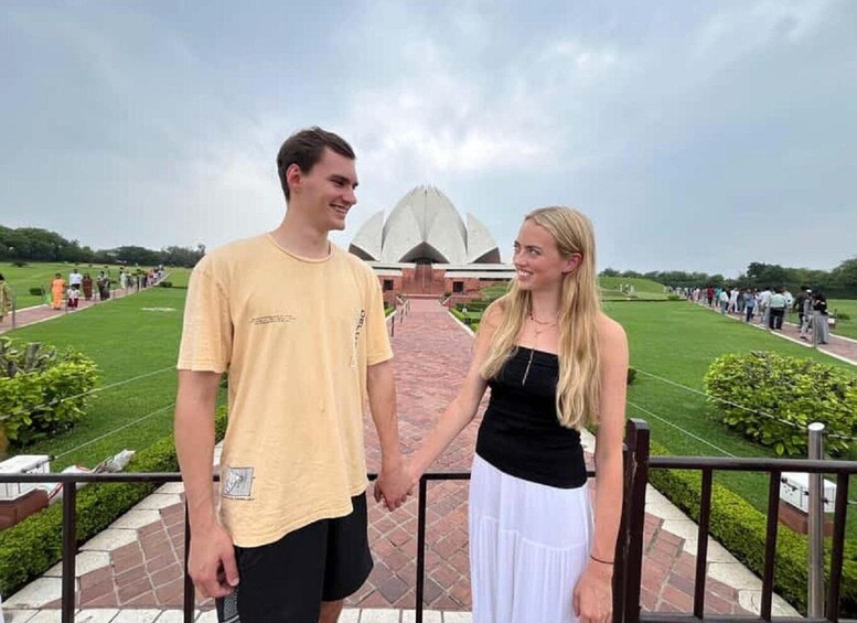 A couple holding hands in front of a large white building with a unique architectural design, surrounded by a well-maintained lawn and a paved walkway. 5