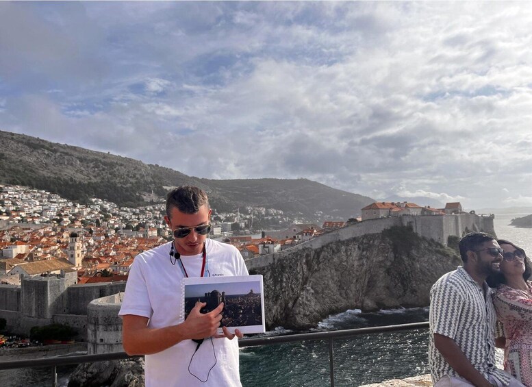 A coastal city with a historic fortification, a person holding a photo album, and a couple sitting on a railing. 5