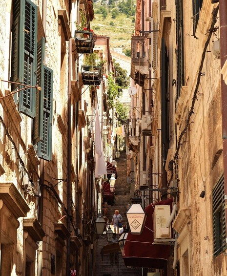 A narrow street flanked by old buildings with shutters and hanging laundry. 4