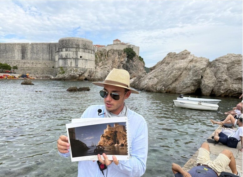 A person holding a photo album with a picture of a coastal fort. 1