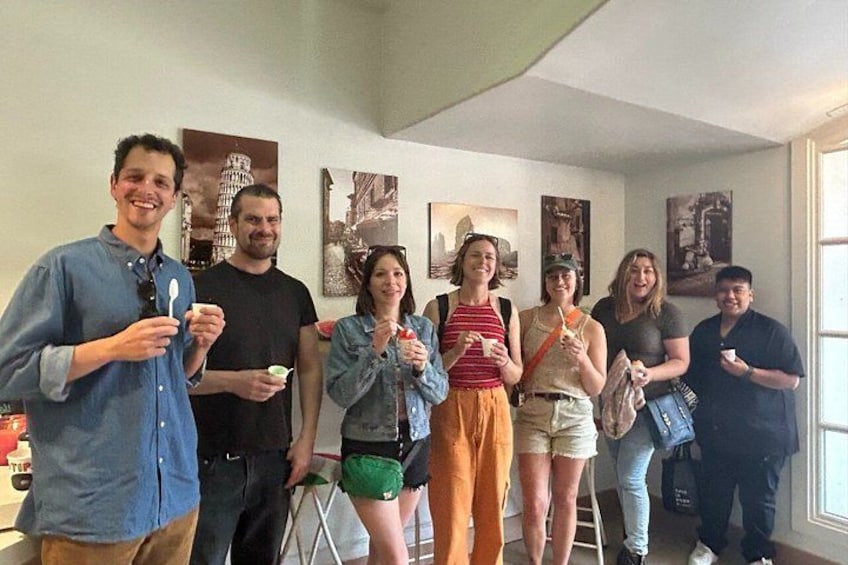 A group of people indoors, some holding food items, with a cityscape painting in the background. 4