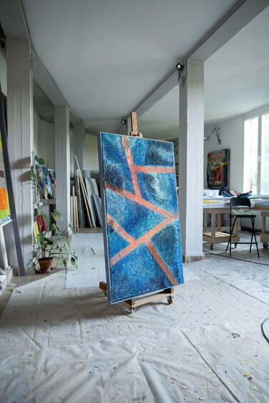 An art studio with a large painting on an easel, a potted plant, and various art supplies scattered around. 2