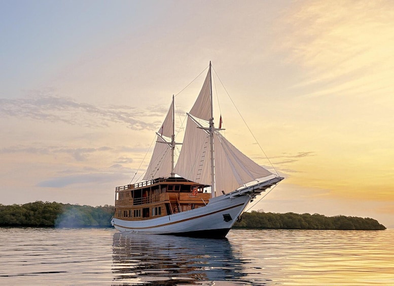 A large sailing ship with multiple masts and sails, anchored in calm waters with a sunset sky in the background. 1