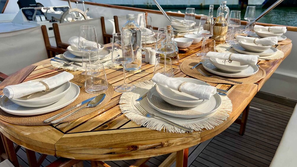 A wooden table set for a meal on a boat with plates, glasses, and cutlery. 2