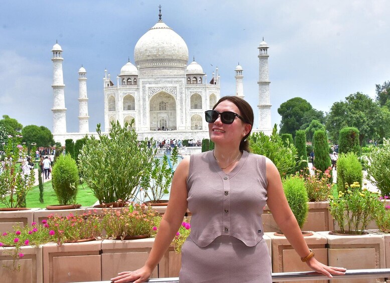 A person standing in front of the Taj Mahal with its domes and minarets visible. 4