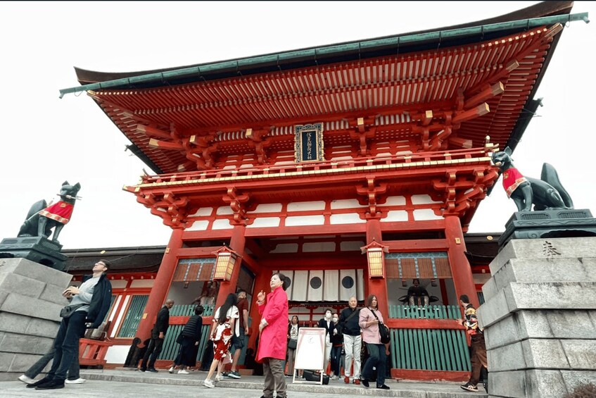 A traditional Japanese building with a red roof and wooden beams, surrounded by stone statues and a crowd of people. 3