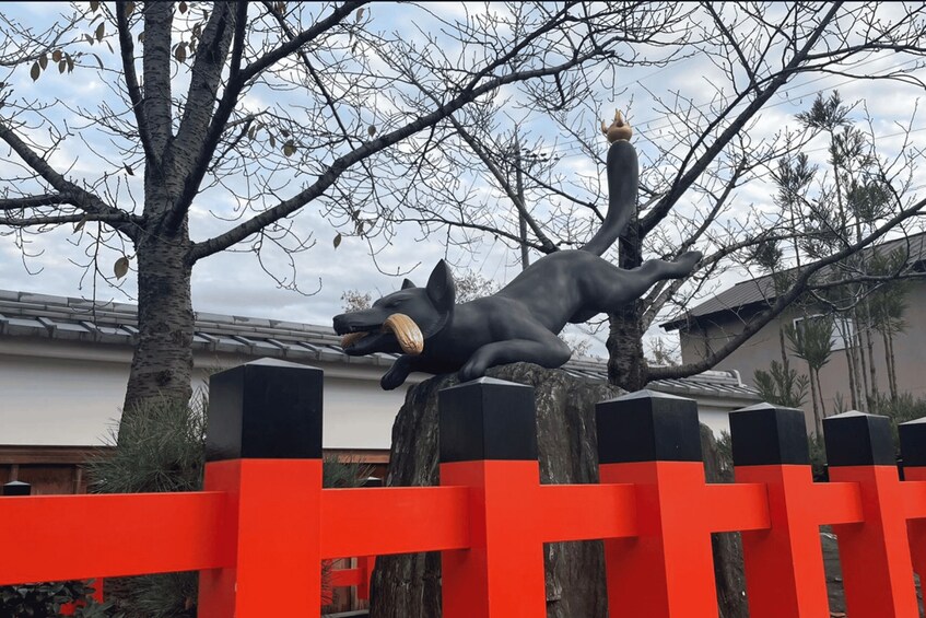A statue of a black panther with a ball in its mouth, positioned on a red fence with trees and buildings in the background. 2