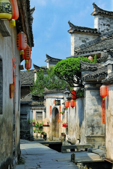 A narrow alleyway with traditional architecture, including tiled roofs and hanging red lanterns. 1