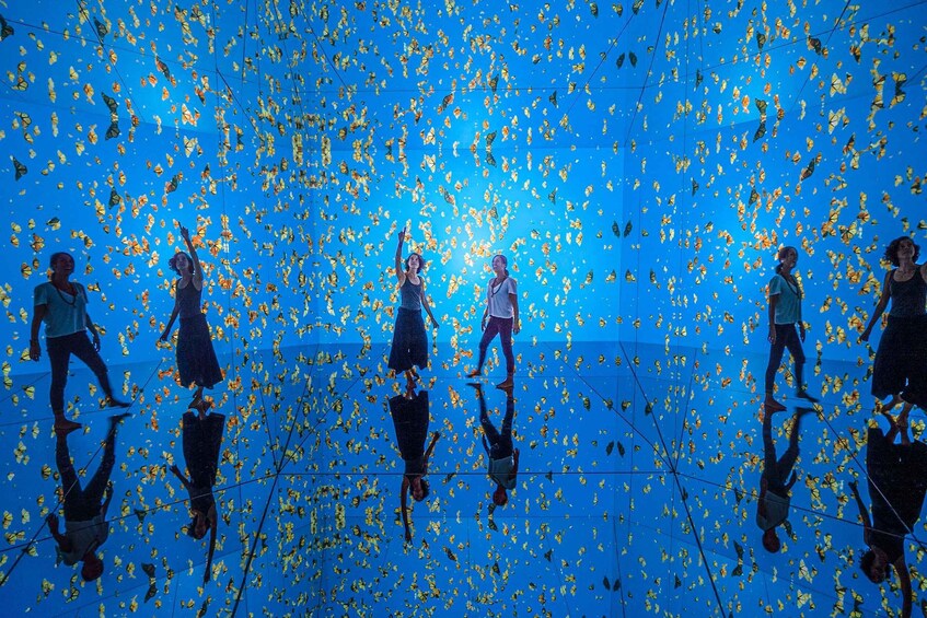 A group of people walking on a reflective floor with a blue background and yellow butterflies. 1