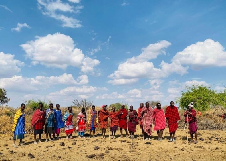 A group of people in traditional attire standing in a dry, open landscape with sparse vegetation and a clear sky. 3