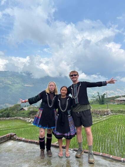 Three people standing on a terrace with a mountainous landscape in the background. 1