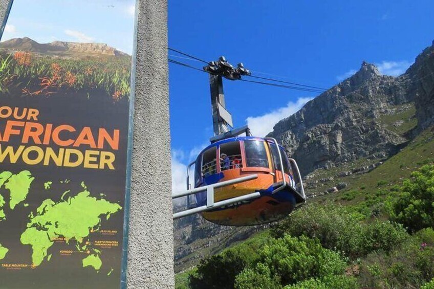 Een kabelbaan in een bergachtig gebied, met een poster die 'Ons Afrikaanse Wonder' adverteert. 2