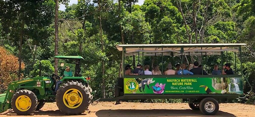 A green tractor pulling a covered cart with people seated inside, labeled 'Nauyaca Waterfall Nature Park.' 4
