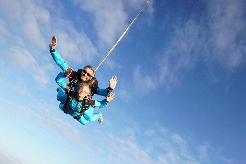 Two people skydiving with parachutes against a clear blue sky. 5