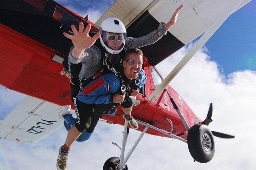 Two people in parachutes attached to a red and white aircraft. 1