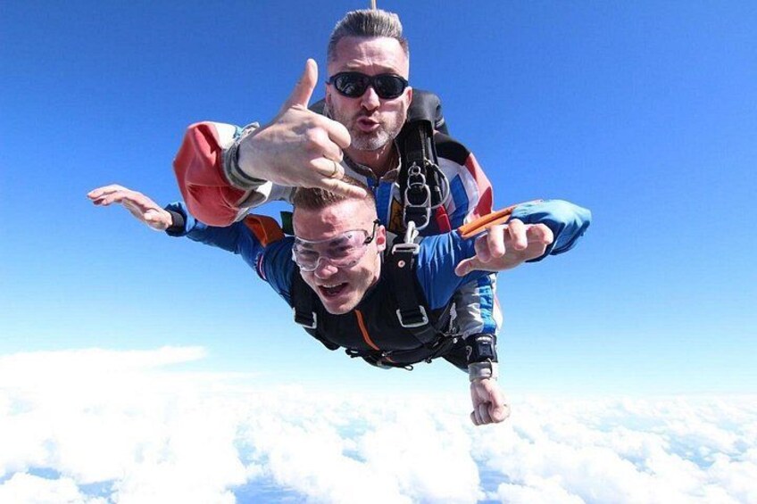Two people skydiving with parachutes above a cloud-covered landscape. 2