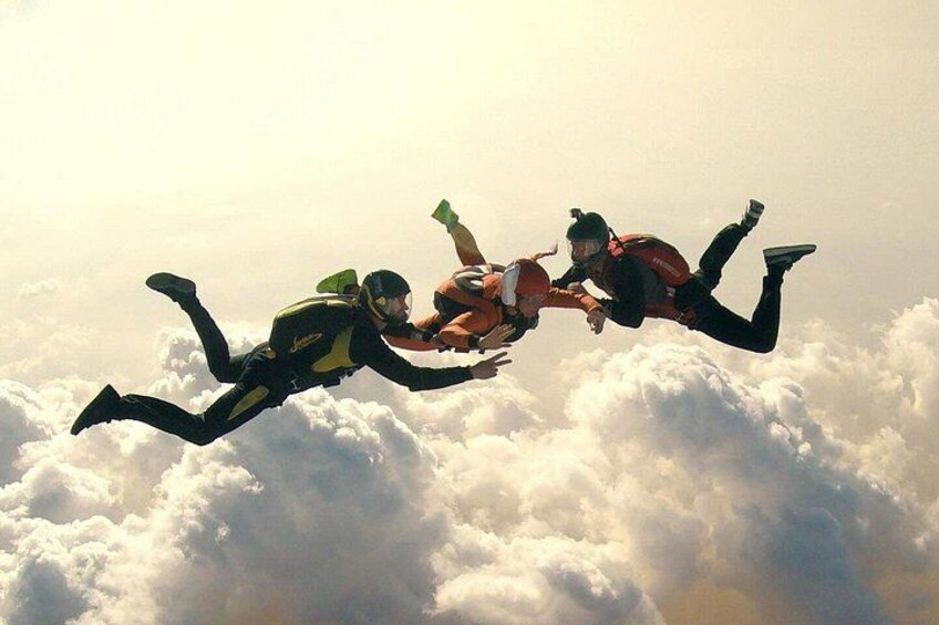 Three skydivers in freefall above clouds. 4