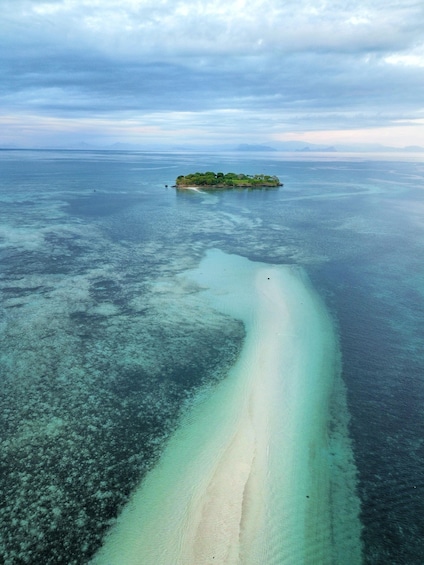 An aerial view of a small island surrounded by clear turquoise waters with a sandy beach. 1